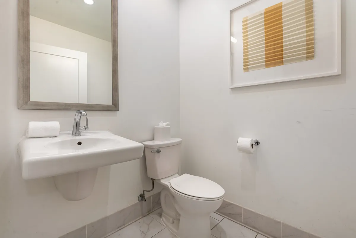 A compact half bath featuring a wall-mounted sink, modern toilet, and tasteful framed artwork. The design is minimalist and tranquil, ideal for quick freshening up.