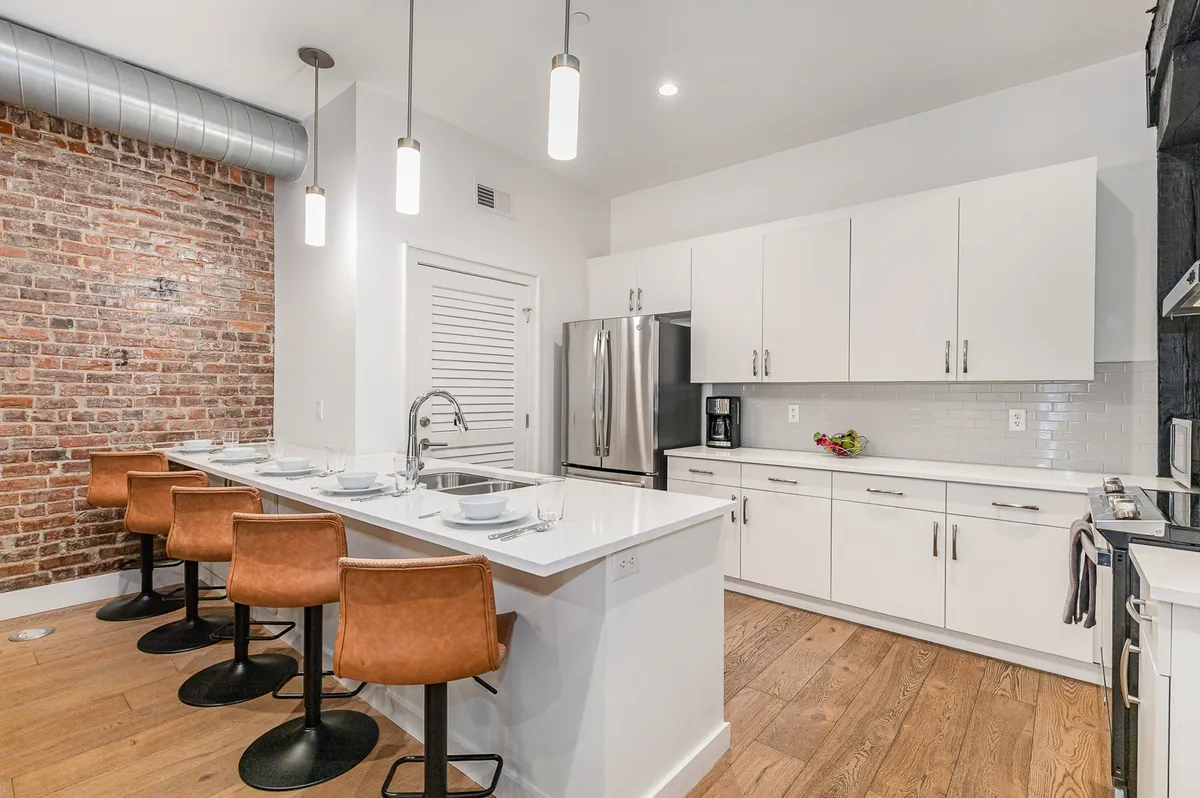 A stylish kitchen with an exposed brick wall, kitchen island with seating, modern cabinetry, and high-end appliances. The space has a contemporary and social vibe, ideal for hosting brunches, late-night snacks, and festive drinks.