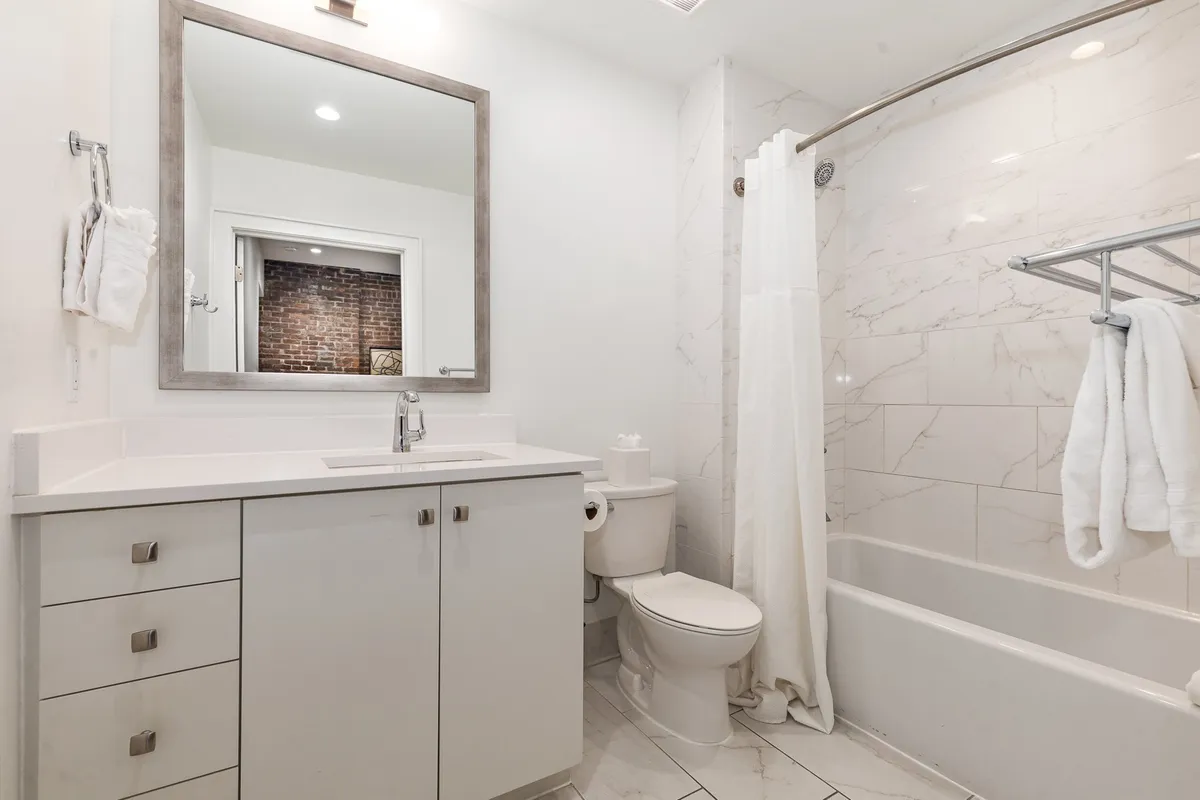 A contemporary bathroom with a wide mirror, sleek modern sink, elegant marble tiles, and a neutral shower curtain. The space feels airy and inviting, reflecting a sense of luxury and comfort.