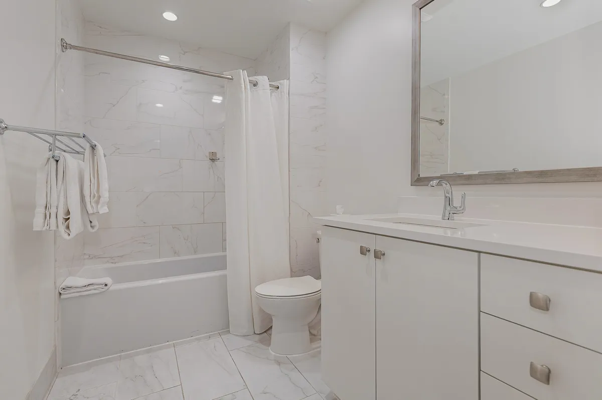 This image depicts a modern, serene bathroom featuring a deep bathtub, a well-lit vanity, a large mirror, and plush towels. The setting is bright and clean, emphasizing a relaxing atmosphere perfect for unwinding after a busy day.